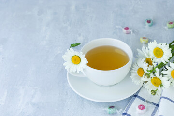 Herbal chamomile tea with fresh chamomile flowers in a white cup and saucer on a light background. Copy space.