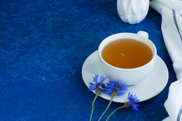 Herbal tea in a white cup and saucer on a blue background. Bouquet of cornflowers. Healthy lifestyle. Horizontal position.