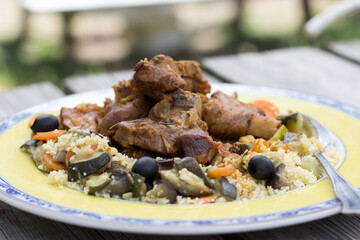 lamb dish with cous cous served on a yellow plate on a wooden table outdoors