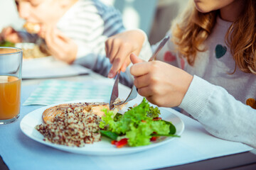 Close up photo of hands of child girl eating healthy dinner with salad, quinoa and fish