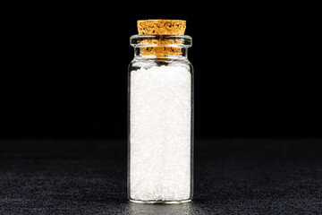 Macro shot of not ground sea salt in a small glass bottle closed with a cork, isolated on a black background.