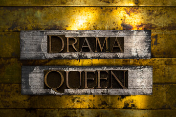 Drama Queen text formed with real authentic typeset letters on vintage textured silver grunge copper and gold background