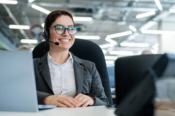 A happy female support operator is sitting at a desk and answering calls. Beautiful smiling woman...
