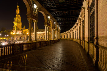 Spanish Square - A wide-angle night view of illuminated the north wing of the semi-circular brick building, as seen from ground-level portico, at Spanish Square - Plaza de España, Seville. Andalusia,  - obrazy, fototapety, plakaty