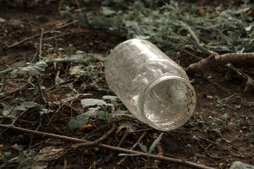 Empty dirty glass jar on the ground among grass and branches. Concept: environmental pollution, difficult to recycle waste, environmental problem. Selective focus, vintage toning.