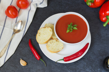 Summer diet cold gazpacho soup of tomato in a white bowl, pepper and herbs on a black background top view . Sliced bread for snacks. Ice for cooling. Vegetarian food