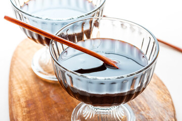 Organic black cane molasses in a glass bowl close-up on a white background.