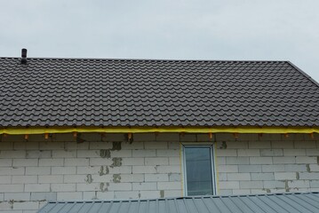 part of a white brick house with a window under a brown tiled roof against a gray sky
