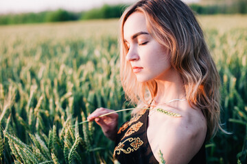 Young, slender girl embroidered dress in a large wheat field at sunset