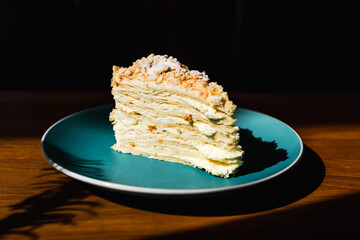 A slice of napoleon cake on a blue plate, direct natural light