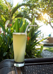 .a glass of juice on the edge of the table on the street terrace, overlooking the pool and tropical plants. Indonesia, Bali