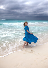 woman with long hair fluttering in the wind in a blue dress on the shore of a stormy sea on a sandy beach (Cuba, Varadero)