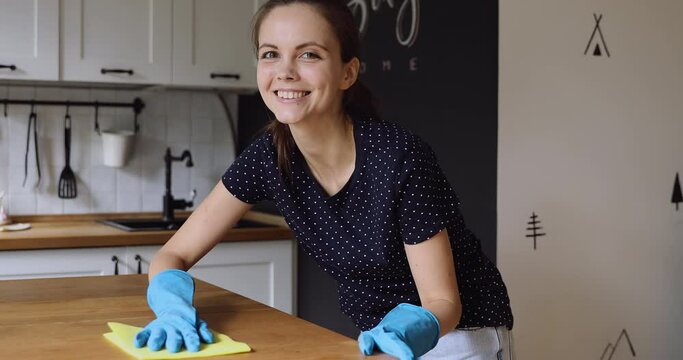 Young housewife do chores wear rubber protective gloves use rag cleans wooden surface of kitchen table enjoy process. House cleaning services worker work with effective home cleaning products concept