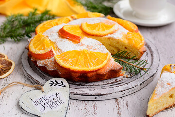 Close up composition of homemade orange pie, white cup with tea and decorative hearts on a light shabby table.