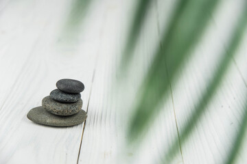 Pyramids of gray zen pebble meditation stones with green leaves on white wooden background. Concept of harmony, balance and meditation, spa, massage, relax