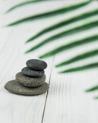 Obraz na płótnie Canvas Pyramids of gray zen pebble meditation stones with green leaves on white wooden background. Concept of harmony, balance and meditation, spa, massage, relax