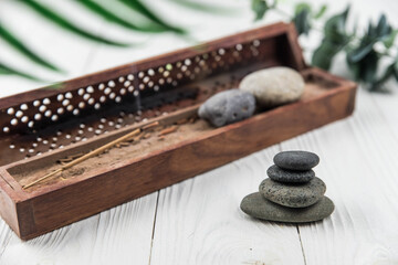 Pyramids of gray zen pebble meditation stones with green leaves and incense stick on white wooden background. Concept of harmony, balance and meditation, spa, massage, relax
