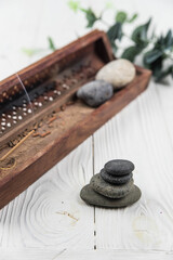 Pyramids of gray zen pebble meditation stones with green leaves and incense stick on white wooden...