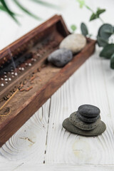 Pyramids of gray zen pebble meditation stones with green leaves and incense stick on white wooden background. Concept of harmony, balance and meditation, spa, massage, relax