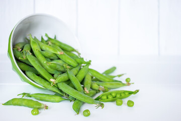 an overturned bowl with fresh green peas spilled in close-up. background with sweet green pea pods.