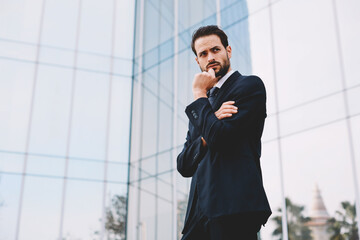 Pensive businessman standing with arm crossed and hand against his mouth looking away