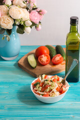 Preparing a vegetarian salad with fresh vegetables and olive oil. Tomatoes, cucumbers are on the cutting Board, a bouquet of flowers in the background