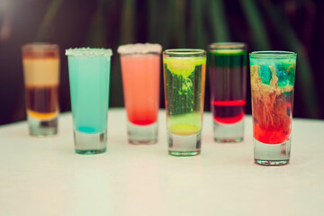 Colorful toned alcoholic shots in white background. Several alcohol shots on sunny bar.