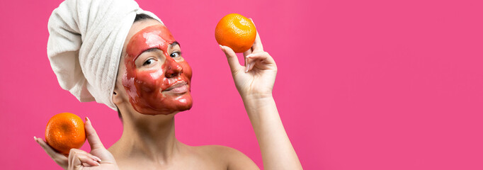 Fototapeta na wymiar Beauty portrait of woman in white towel on head with red nourishing mask on face. Skincare cleansing eco organic cosmetic spa relax concept. A girl stands with her back holding an orange mandarin.