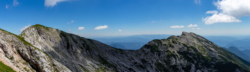 Panorama of the mountain peaks in European Alps, with blue sky in the background and man walking to the top. 