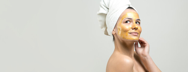 Beauty portrait of woman in white towel on head with gold nourishing mask on face. Skincare cleansing eco organic cosmetic spa relax concept.