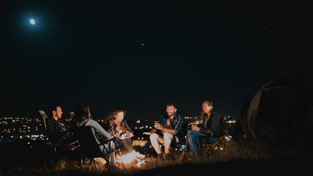The group of friends have fun near the night campfire