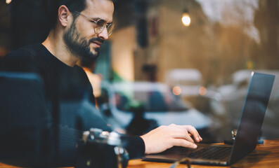 Bearded entrepreneur male in glasses dressed in black sweater reading news checking email and...
