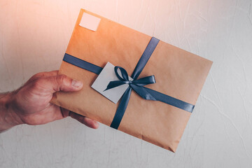 A man's hand holds an envelope with a stamp and a blank label, with a blue ribbon and a bow.