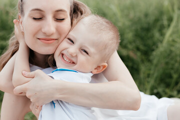 Smiling little boy embracing his happy mother who is sitting with closed eyes in nature. Mother and...