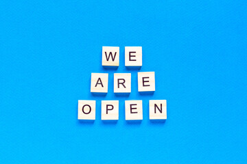 We are open. Wooden cubes with a text message We are open on a blue background. The view from the top. Flat layout. An office, cafe, or store welcomes guests after a coronavirus outbreak.