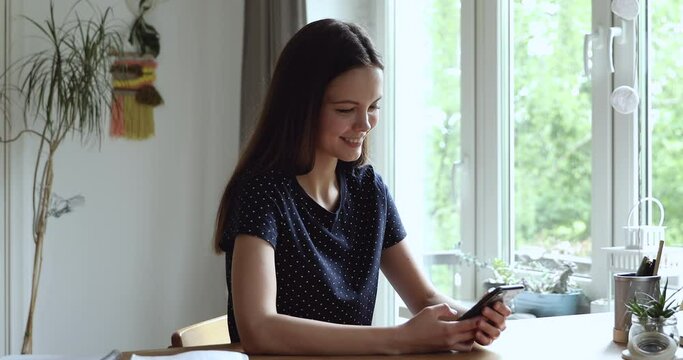 Young woman sitting at desk smiling holding device using smart phone enjoy distant remote communication with friends. On-line chat, websurfing, new application for fun study or business usage concept