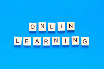 online learning concepts written in wooden letters on a blue background. a top view of a flat layout, a new form of learning, online school