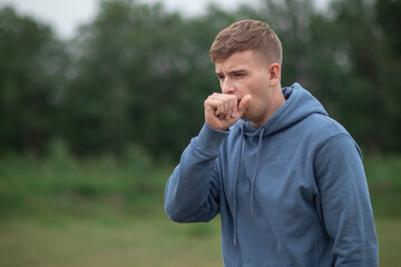 Sick ill guy, young man coughing in his fist, hand, suffering from cough, bronchitis outdoors on...