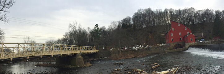 A beautiful view of a red mill by the river, with an old bridge on the left.
