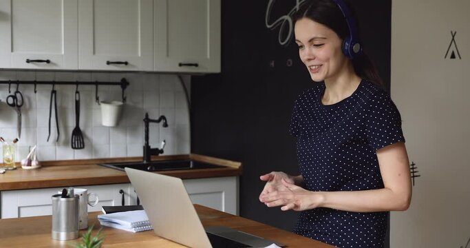 Student girl standing in kitchen wear headphones talking with classmate using video call app. Pass job interview distantly, employee working from home negotiates with client by videoconference concept