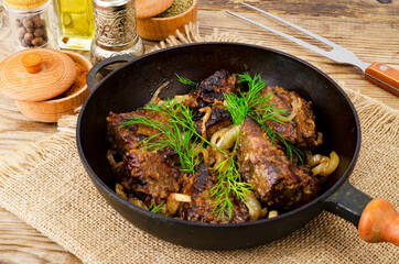 Cast-iron frying pan on wooden table with fried liver.