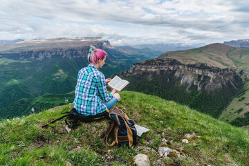 Beautiful young girl reads a book on a background of beautiful mountains. The concept of hanging...