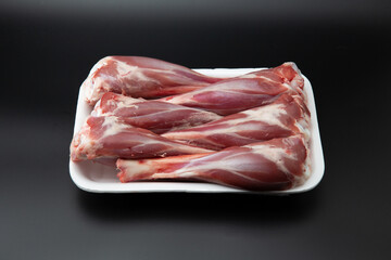 Raw lamb shanks in a white styrofoam container isolated on black background with copy space for text