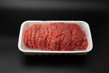 Raw minced (ground) meat in a white styrofoam box isolated on black background with copy space for text