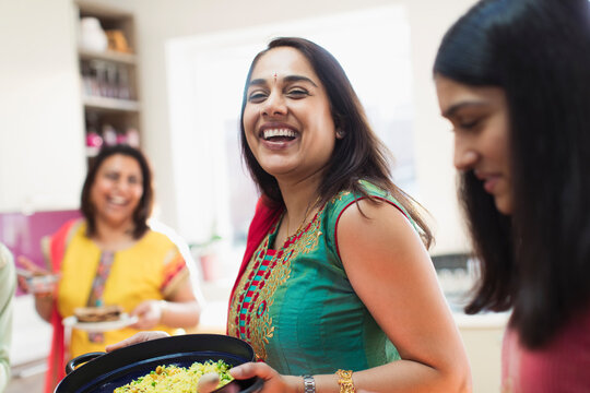 Happy Indian woman in sari preparing food with family in kitchen