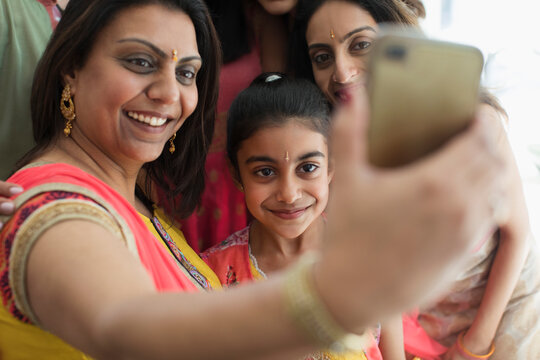 Happy Indian women in bindis and saris taking selfie with camera phone
