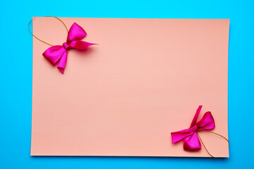 Pure pink piece of paper with a purple bow on a blue pastel background. The concept of a New year. Flat lying style.