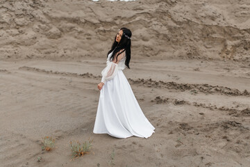 Fototapeta na wymiar beautiful pensive girl in a white puffy dress and a wreath on her head is walking along a sandy quarry