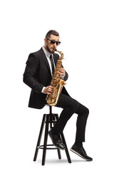 Elegant musician in a black suit playing a saxophone and sitting on a chair