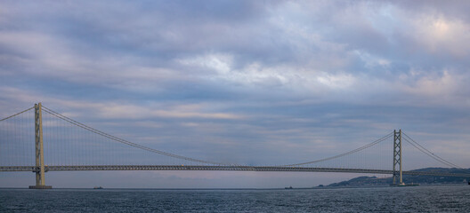 Panoramic view of long suspension bridge under beautiful clouds after sunset